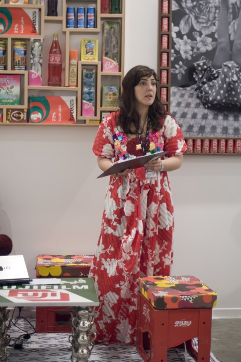 Woman in red floral dress holding tablet at art gallery with colorful shelves behind her