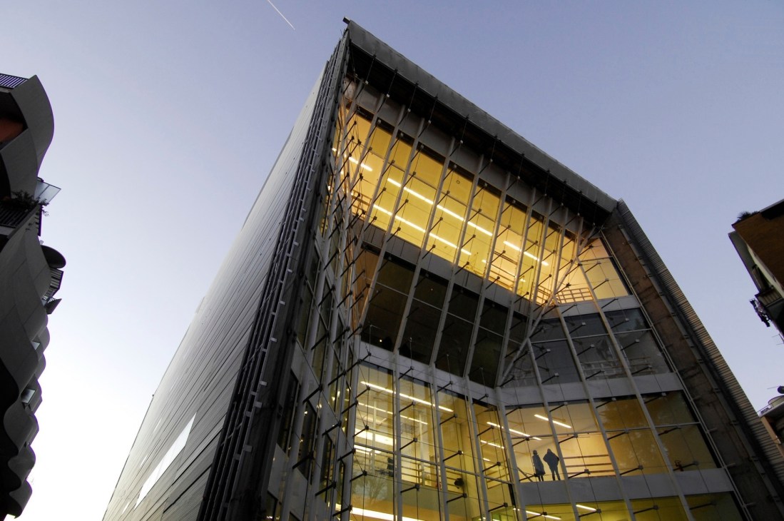 Modern glass-façade museum building illuminated at dusk with yellow interior lighting visible through grid windows.