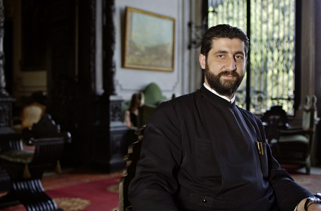 Greek Orthodox priest in dark robes standing in an ornate interior room of Palais Sursock.