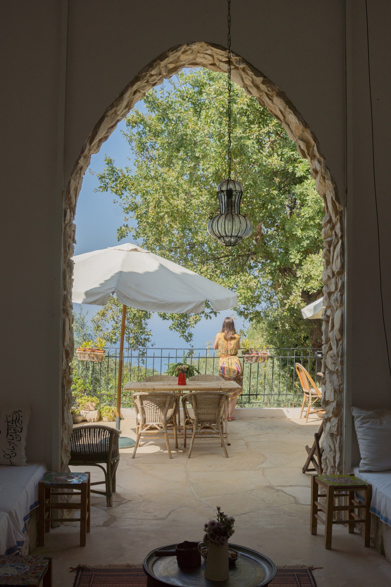 Stone archway framing a terrace at Beit al Batroun with hanging pendant light, outdoor furniture, and Mediterranean Sea view.
