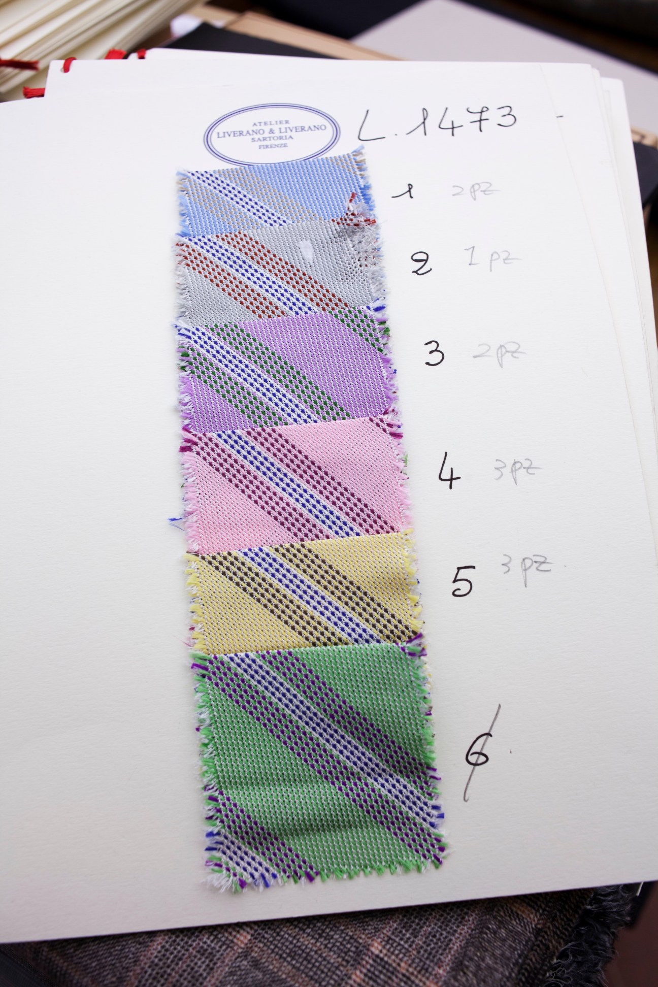 Fabric swatches in various colors pinned to a Liverano & Liverano sartoria document with handwritten notes.