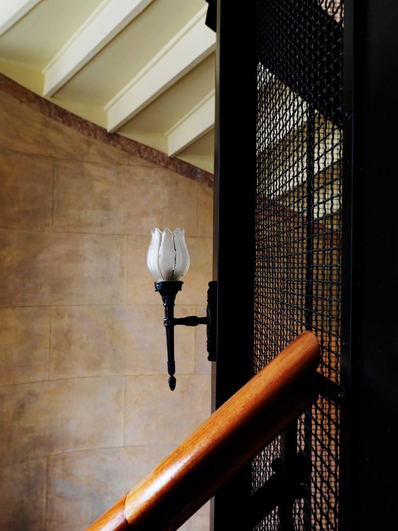 Original sconce light with white tulip-shaped glass shade mounted on stone wall in Block C stairwell