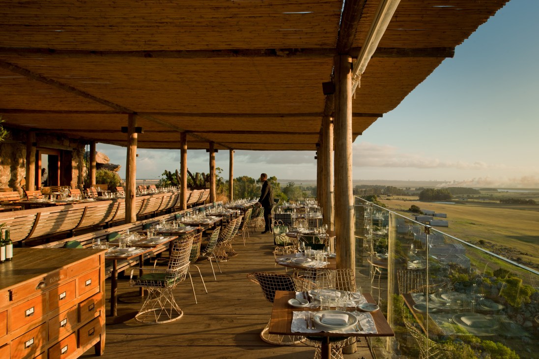 Las Piedras Fasano restaurant terrace with wooden beams, set tables, and panoramic countryside views.