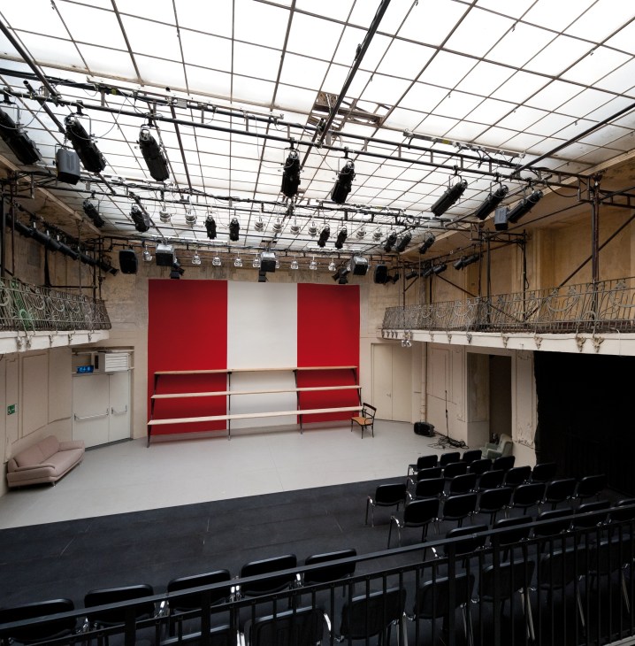 Theater Nestroyhof Hamakom auditorium with red and white backdrop, industrial ceiling, and black seating.