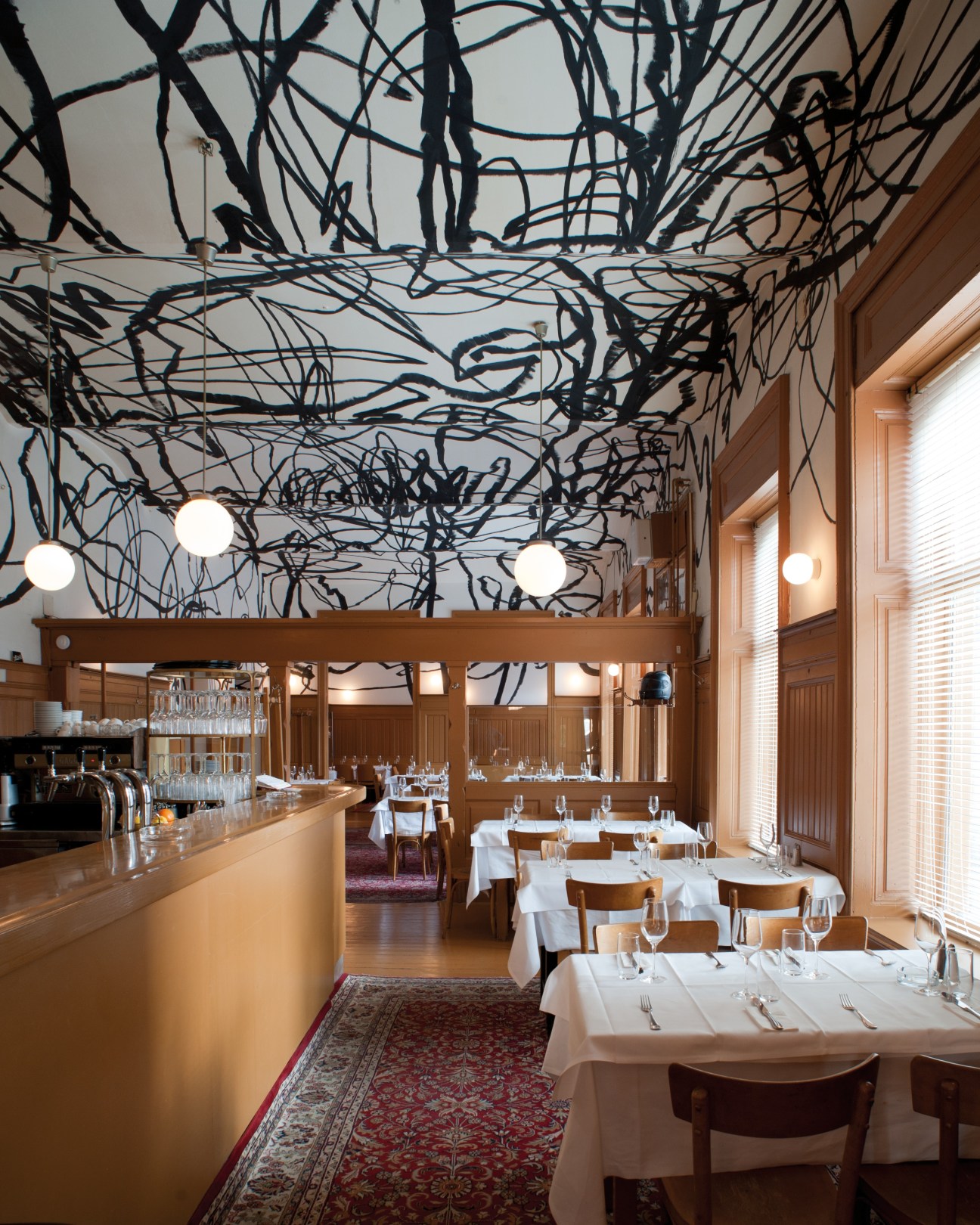 Interior of Skopik + Lohn restaurant with abstract black scribbles on ceiling and wooden furnishings.