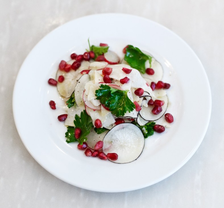 Radish, celeriac and pecorino salad with pomegranates and truffle oil on a white plate.