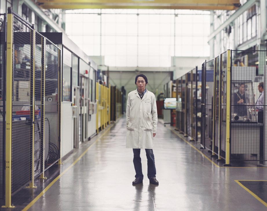 Dr Andrew McGordon stands in a laboratory corridor lined with yellow and black safety-caged equipment at Warwick Manufacturing Group.
