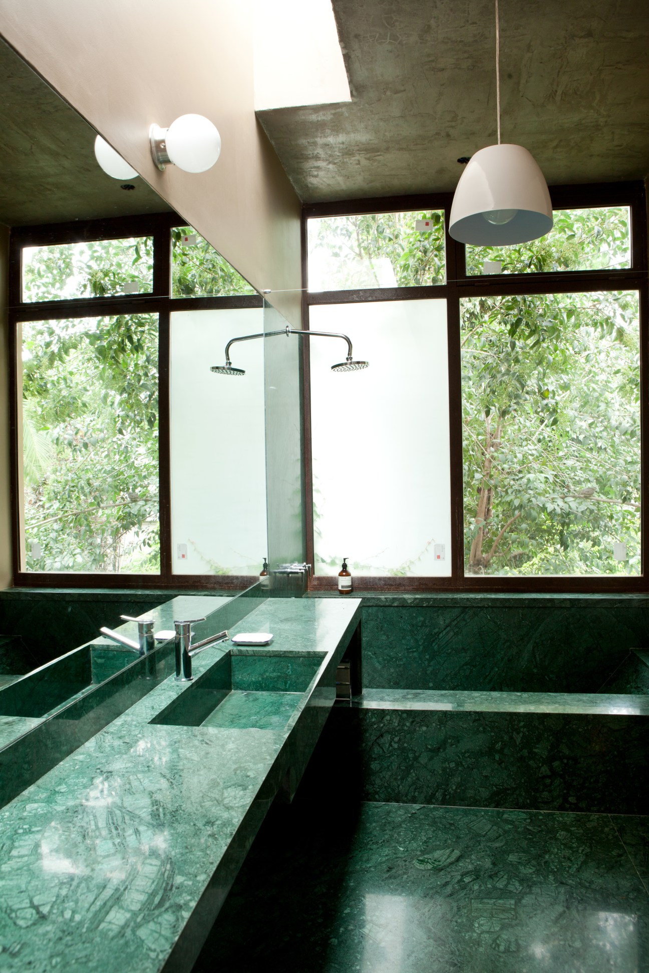 Modernist bathroom with green marble countertops, dual sinks, pendant lighting, and large windows overlooking greenery.