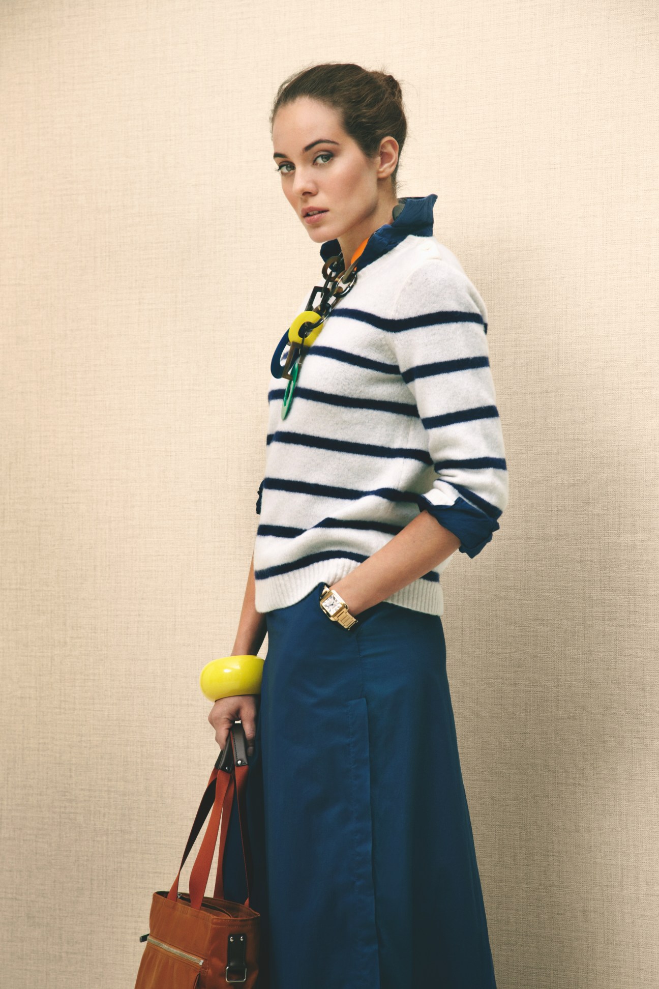 Woman wearing striped knit jumper, navy trousers, and accessories including yellow bracelet and brown leather bag.