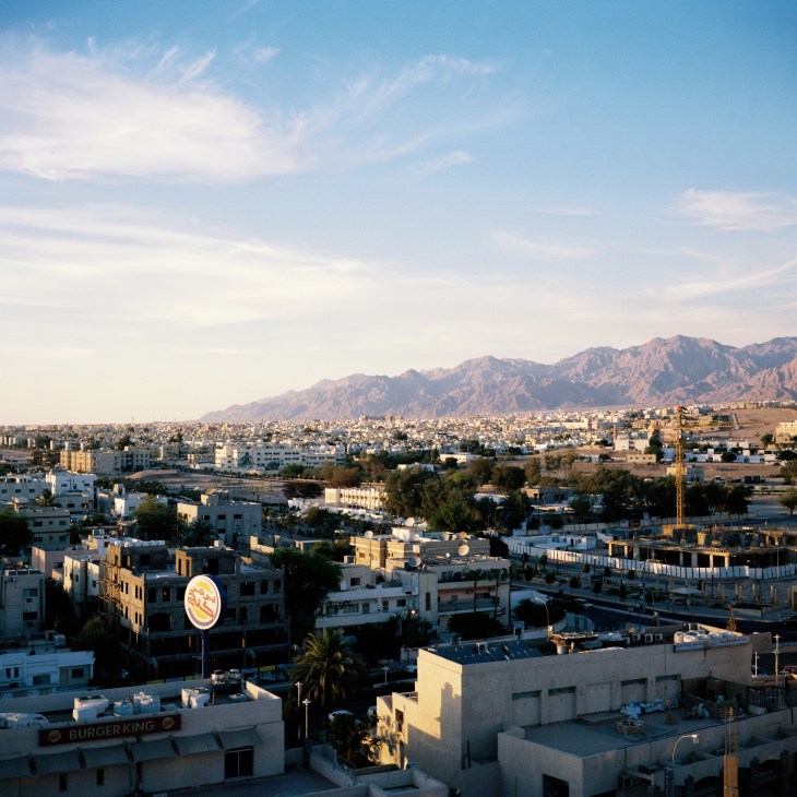 Aerial view of Aqaba showing cityscape with mountains and Edomite Mountains in background under blue sky.