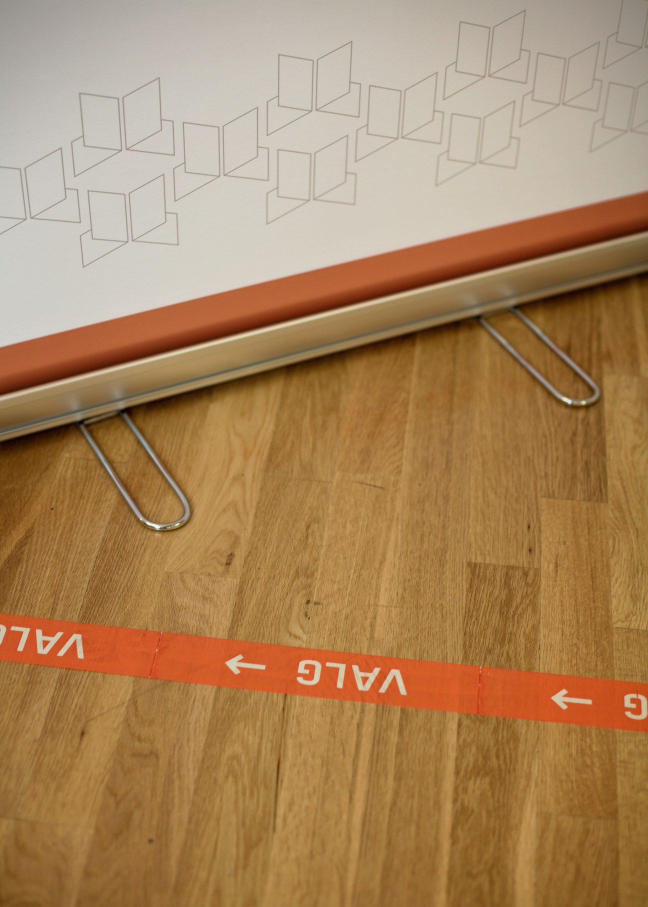 Orange directional tape with arrows and VALLE text guides voters across wooden flooring toward a polling station.
