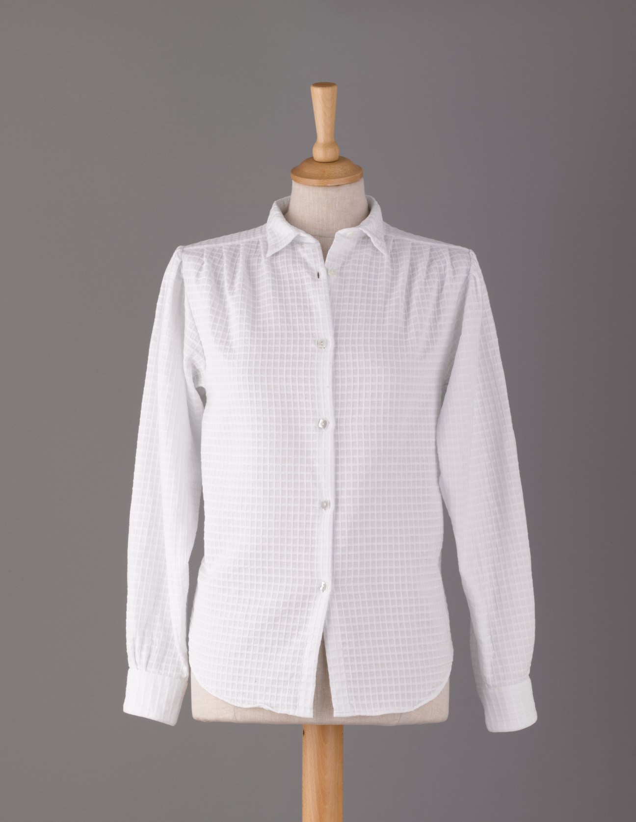 White check button-down shirt on dress form against gray background.