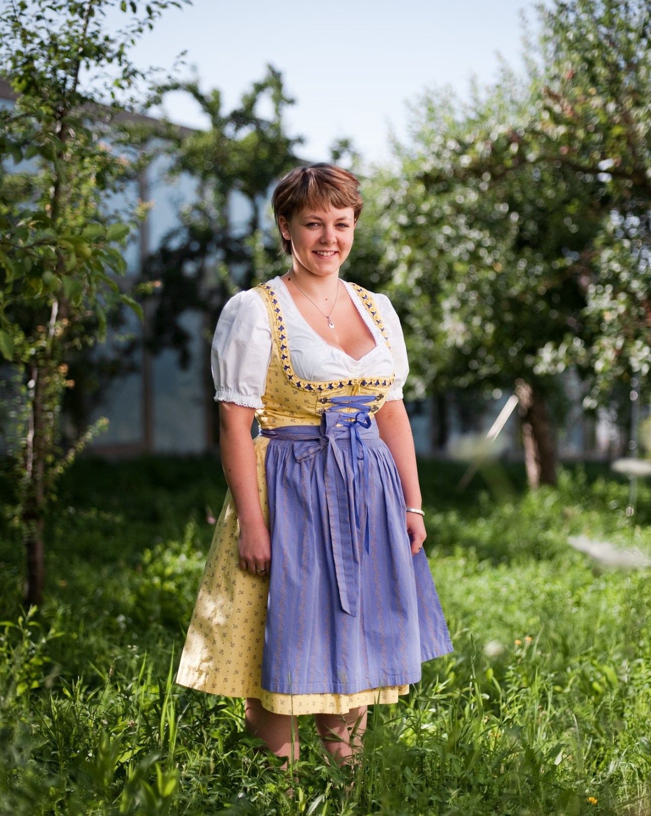 Woman in traditional Bavarian dirndl dress standing in orchard with fruit trees.