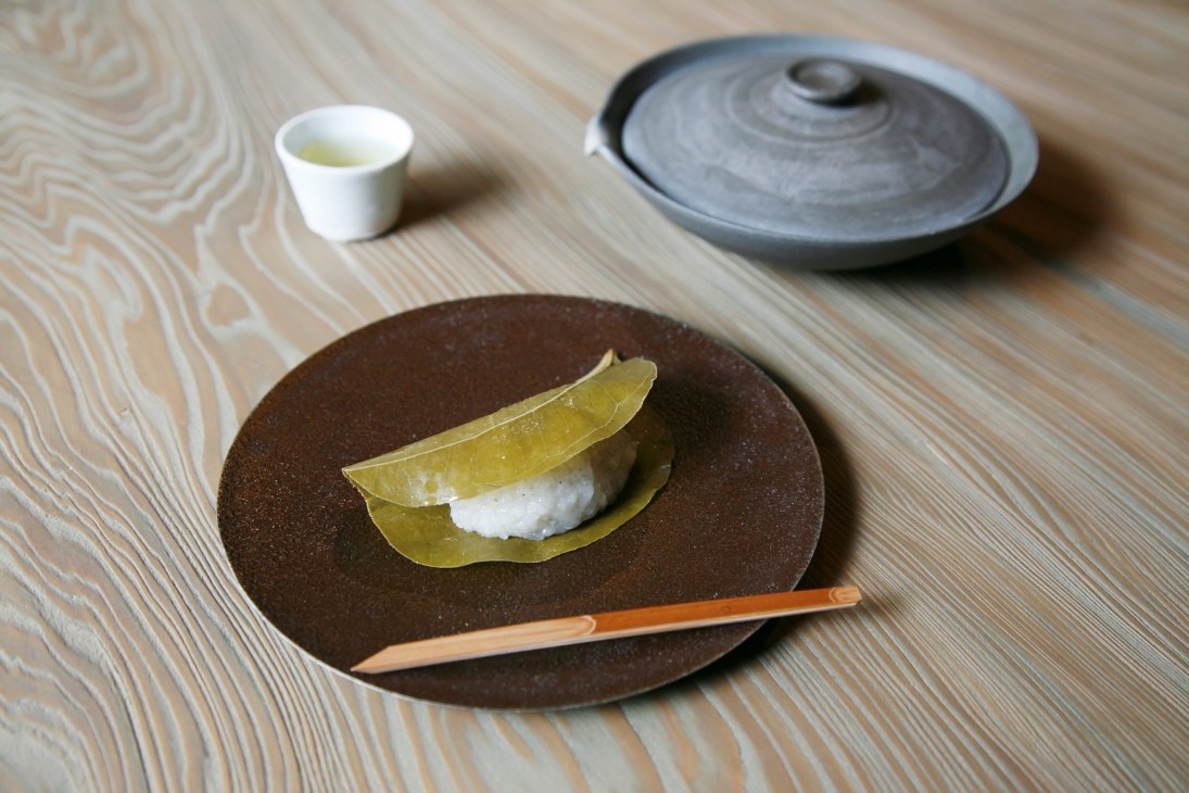 Japanese sweet on a dark plate with tea cup and ceramic vessel on wooden surface at Baishinka Tokyo.