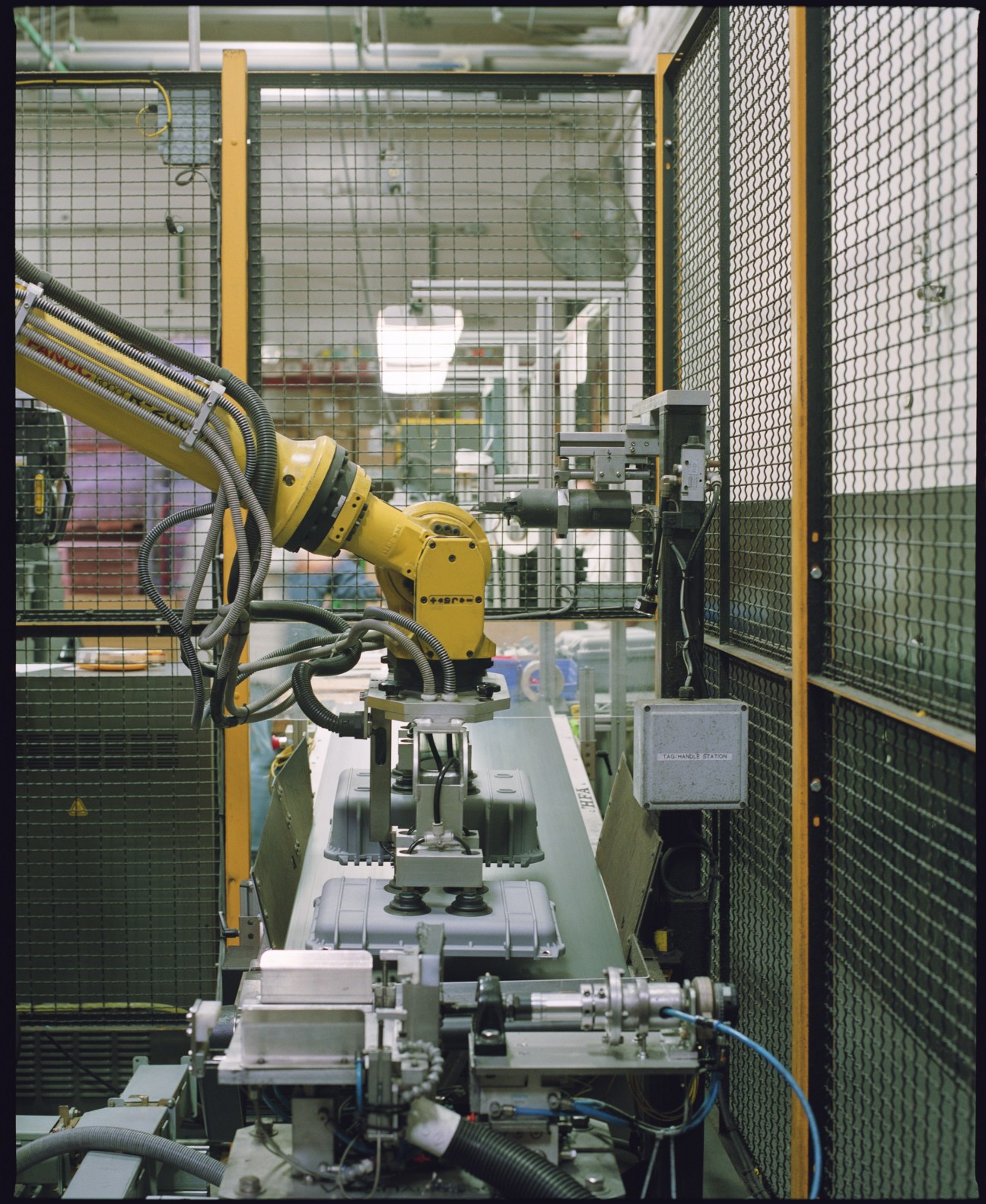 Yellow industrial robot arm drops plastic cases onto a production line at Pelican manufacturing facility.