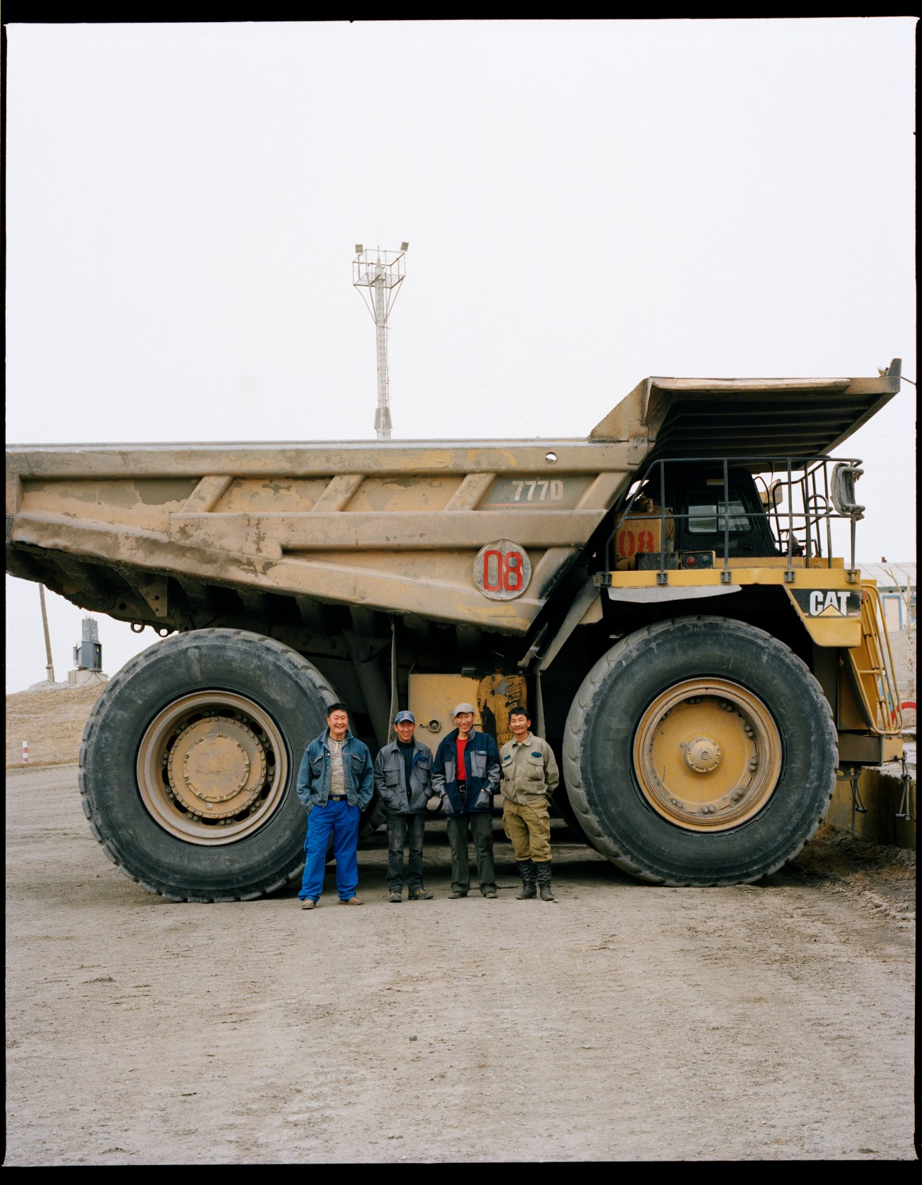 Four workers stand beneath a massive yellow CAT dump truck at Baganuur Mine in Mongolia.