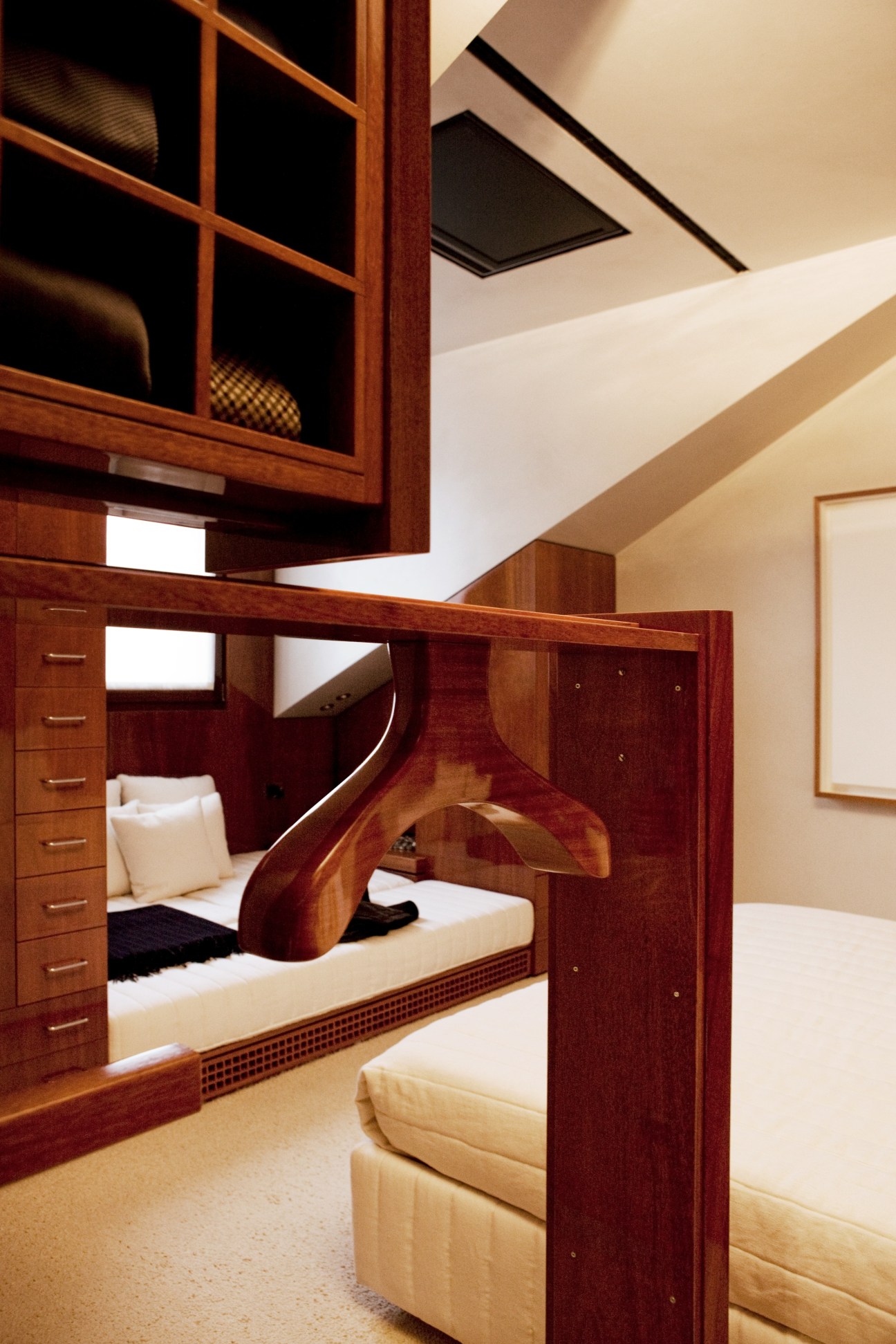 Bedroom with mahogany built-in storage featuring drawers and shelving, cream upholstered seating, and natural skylight.