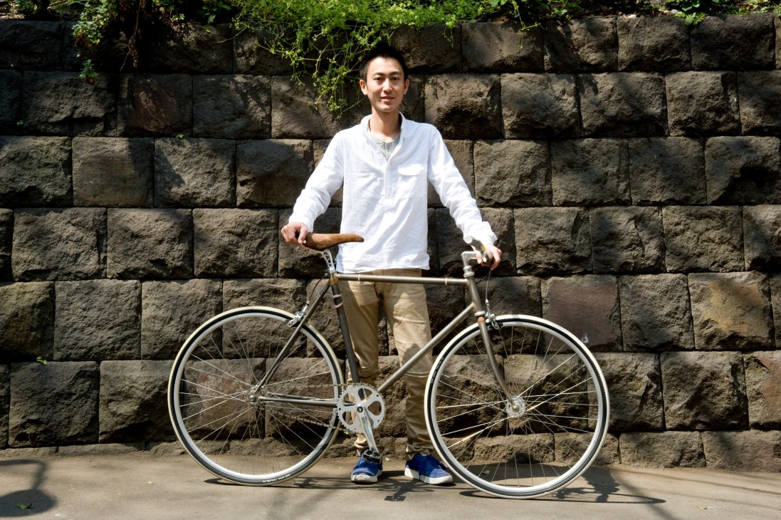 Kei Nakazato, manager of F.I.G. Bike store, posing with a Funriki bicycle against a stone wall.
