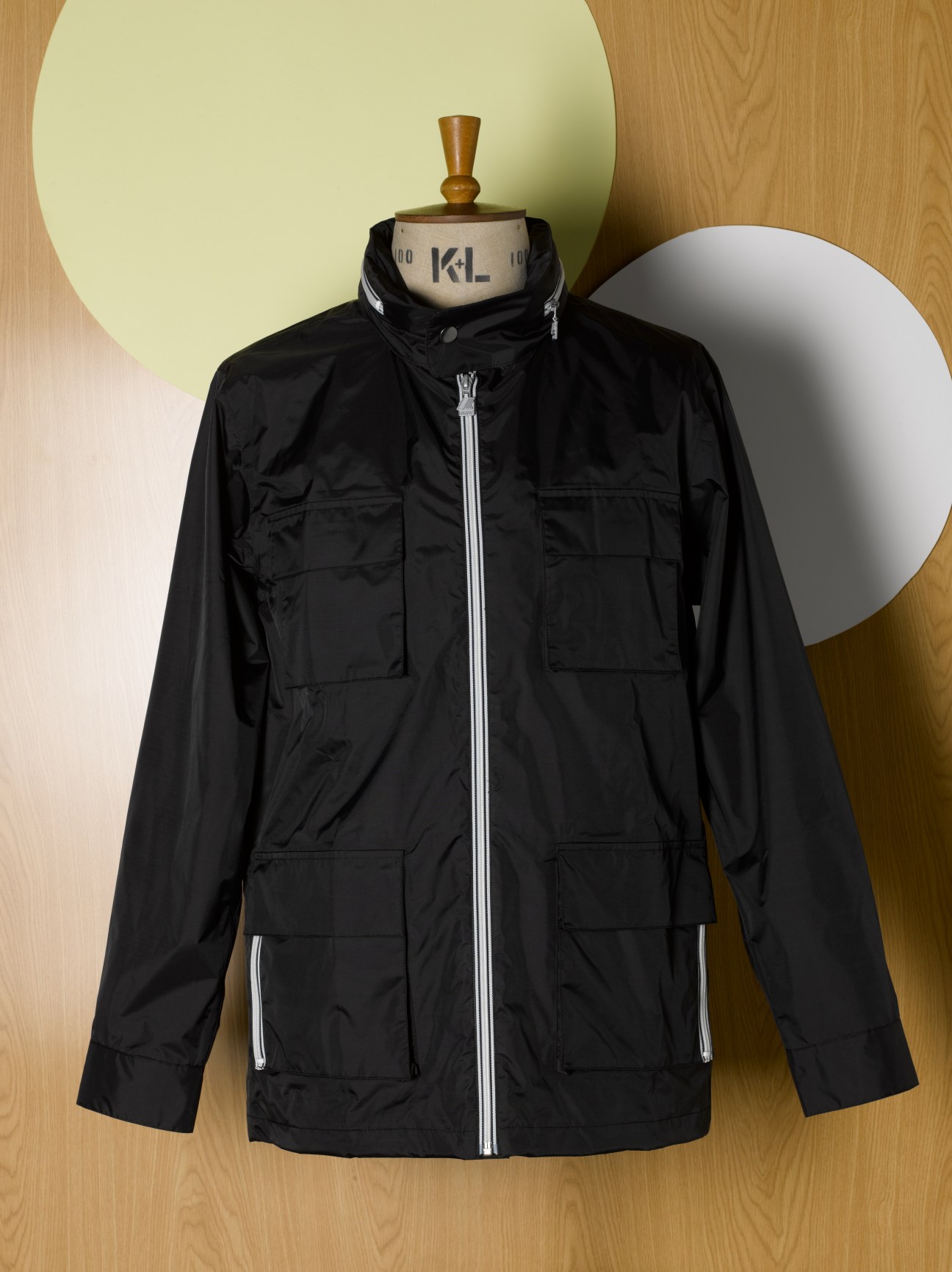 Black APC x K-Way raincoat with contrast zip and roll-away hood on dress form.