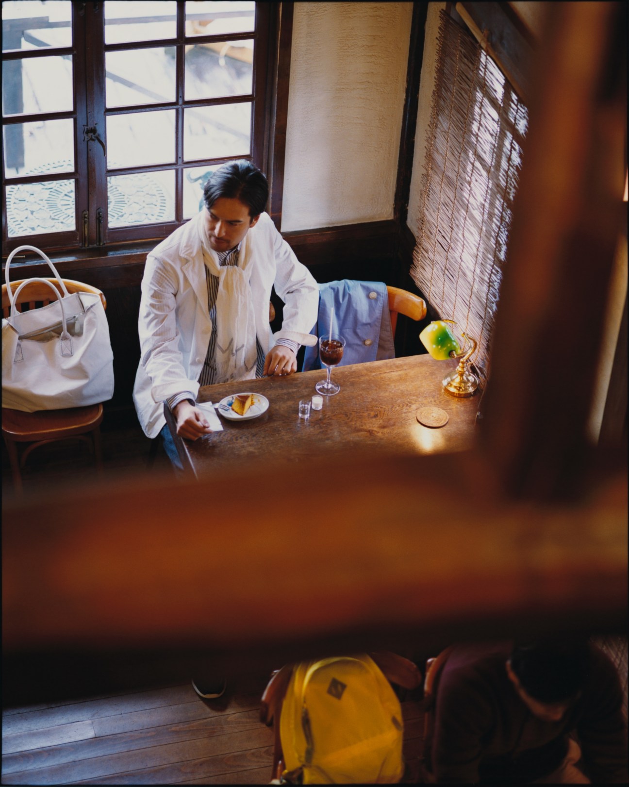 Man in white Bottega Veneta jacket and striped shirt seated at table by window in Hayama interior.