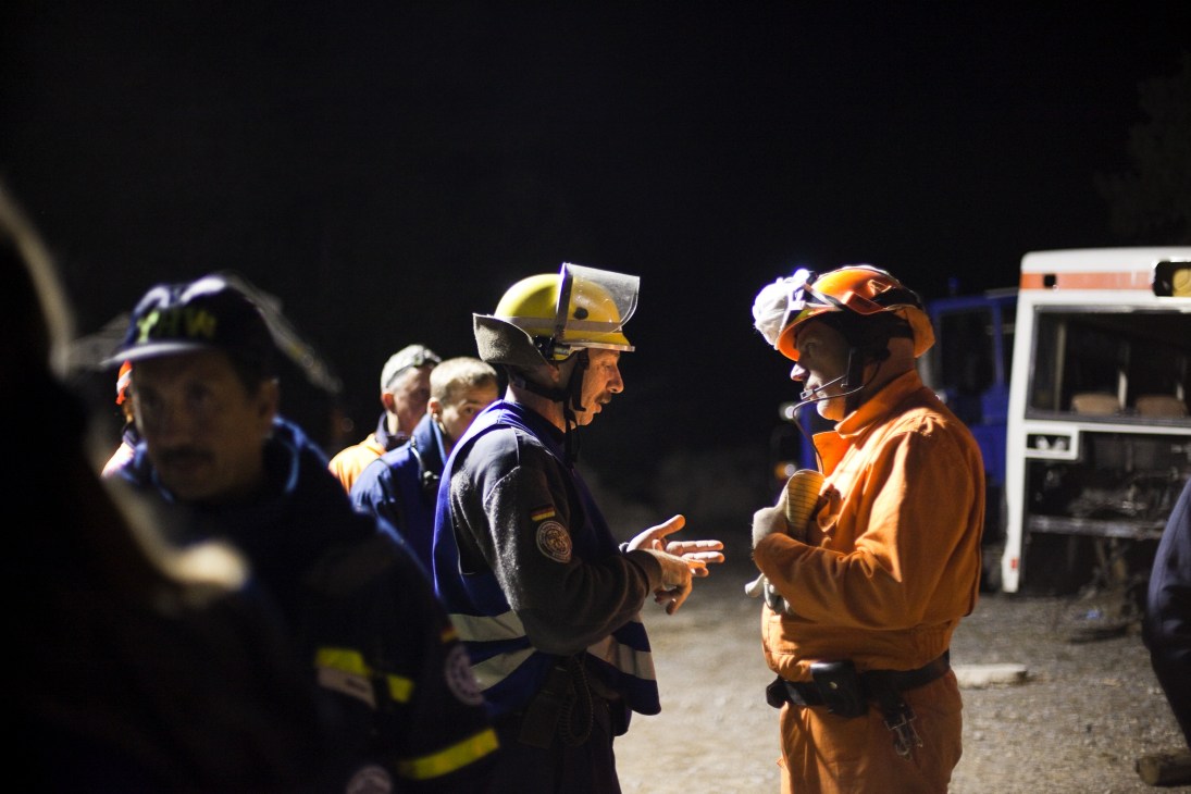 German THW rescue workers in blue uniforms confer with Dutch team members in orange at an international training event at night.