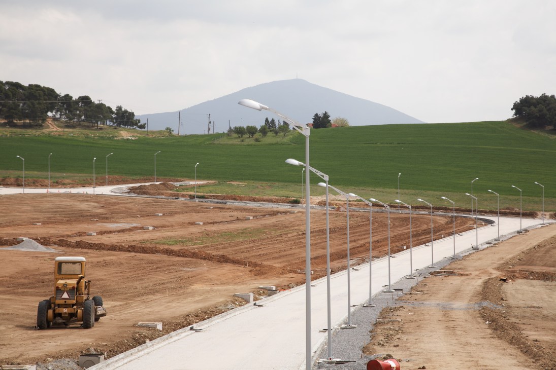 Construction site with earthmoving equipment, street lights, and green hills in background during Technopolis development.