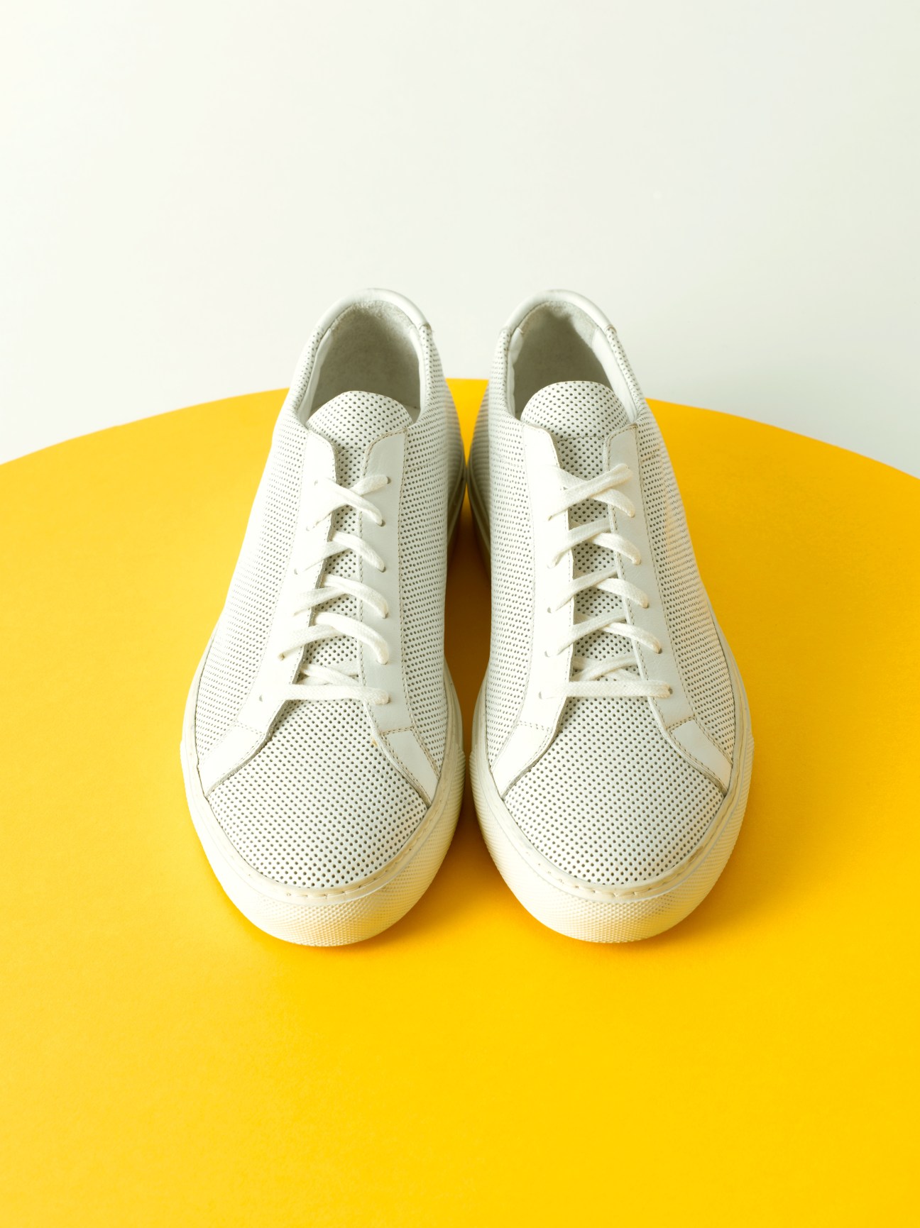 Pair of white Common Projects minimalist sneakers on yellow background.