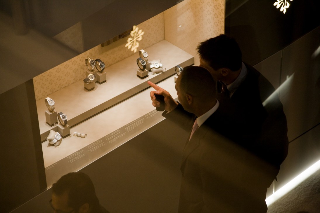 Visitors viewing luxury watches displayed in an illuminated Patek Philippe showcase cabinet.