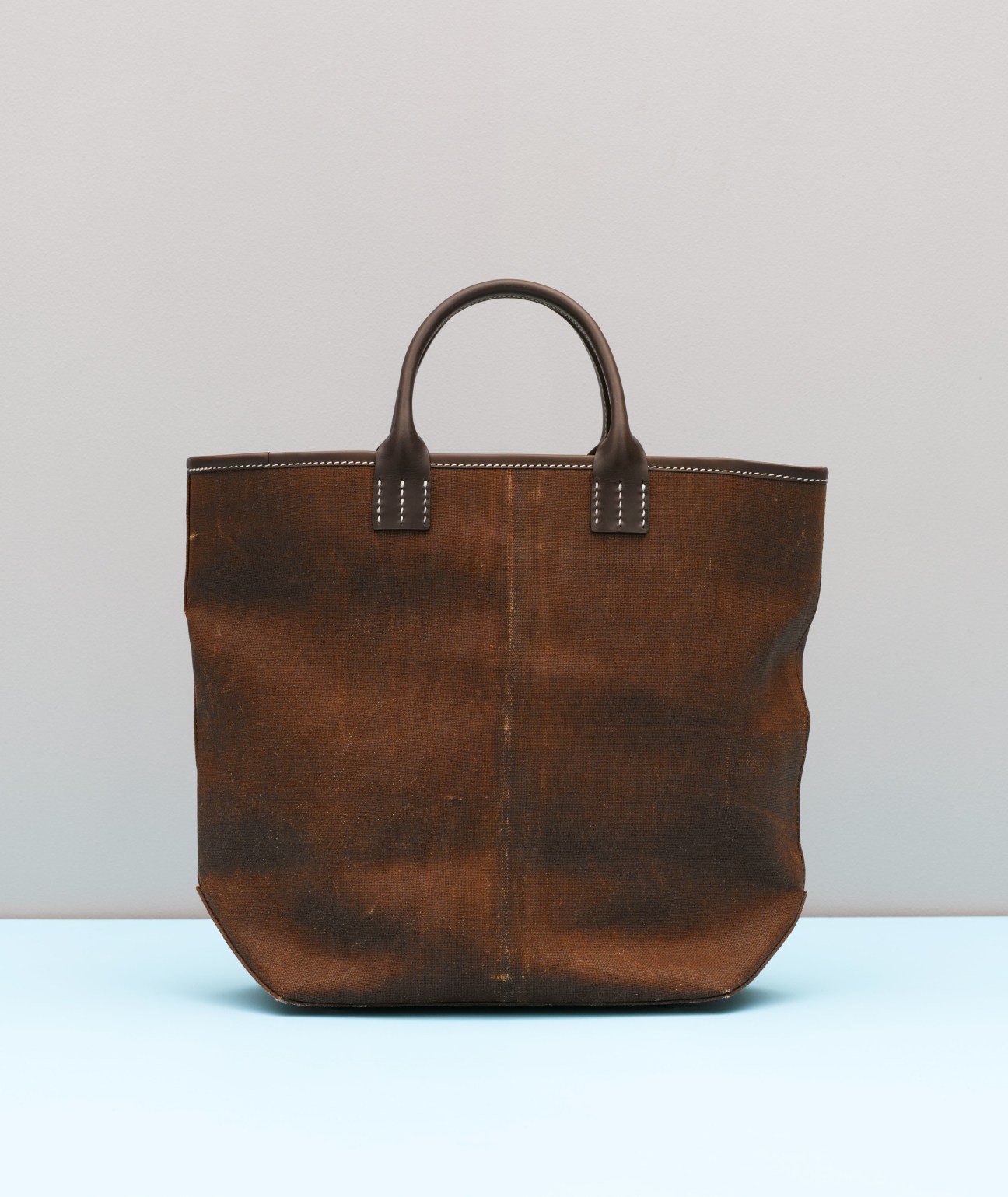 Brown canvas tote bag with leather handles and white stitching detail on light background.