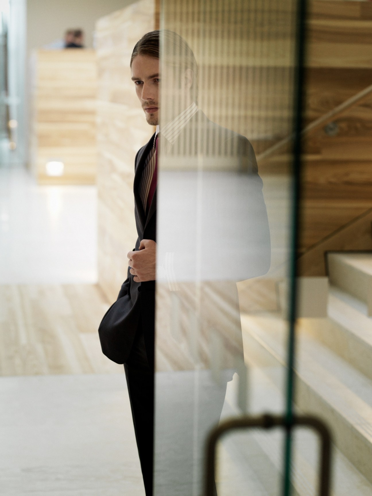 Man in wool/linen suit and cotton shirt by Gieves & Hawkes posing in modern office corridor.