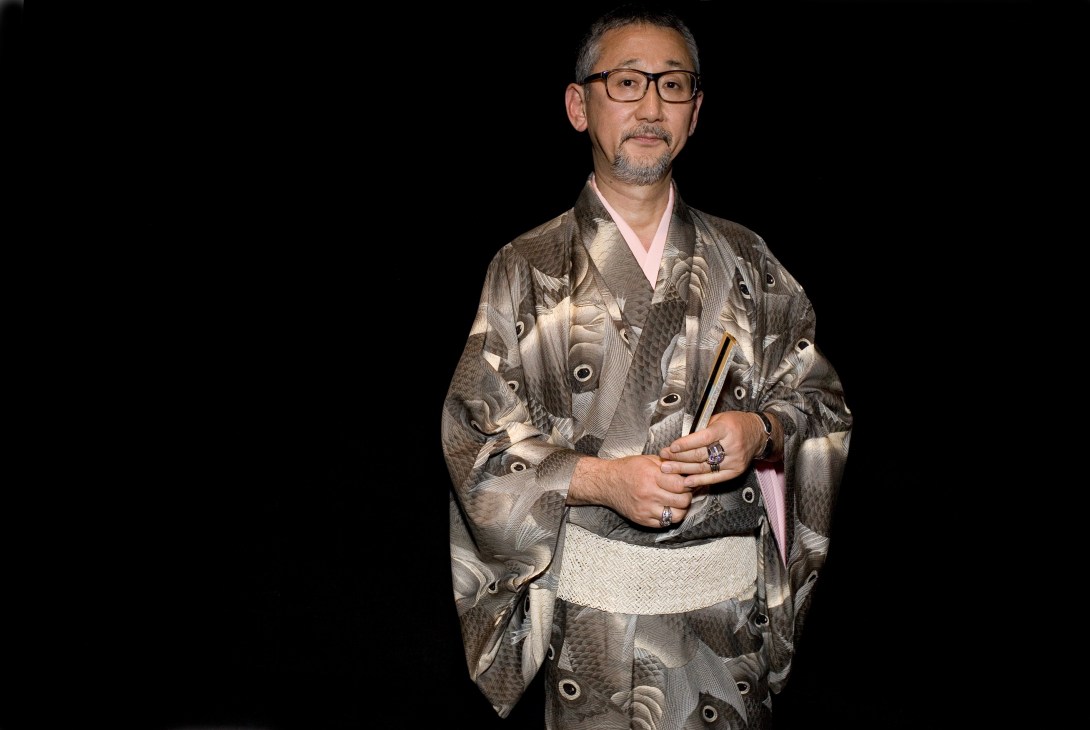 United Arrows chairman Osamu Shigematsu wearing a grey kimono with white motifs and white obi against a black background.