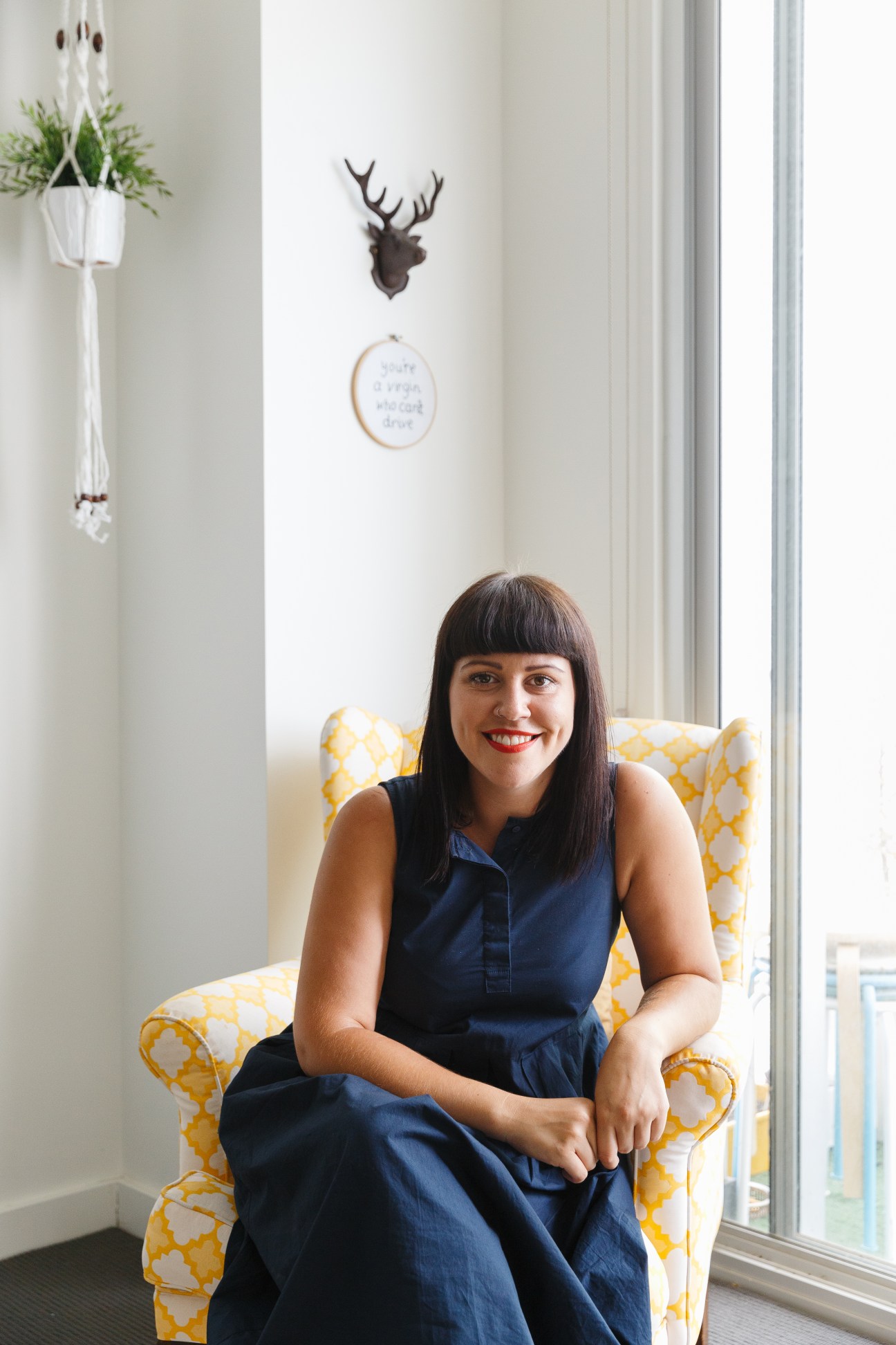 Steph Berndt sits in a yellow patterned chair in her bright one-bedroom Ergo apartment with white walls and modern décor.