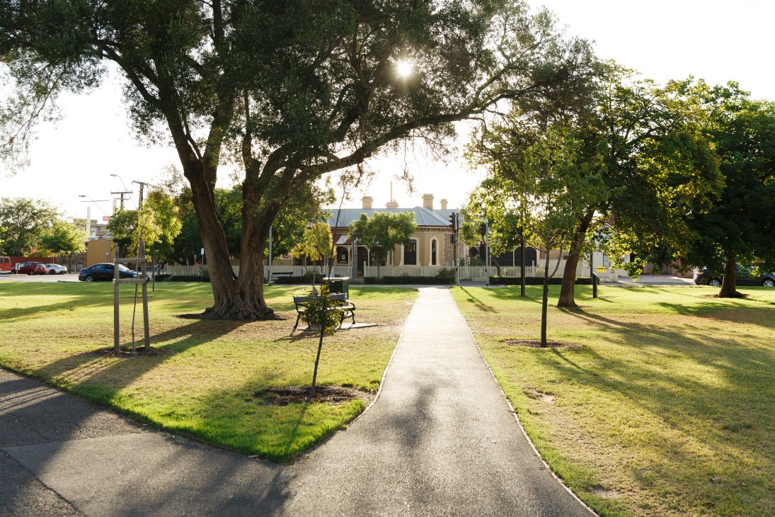 Whitmore Square in Adelaide with leafy trees, manicured lawn, and heritage colonial building in background.