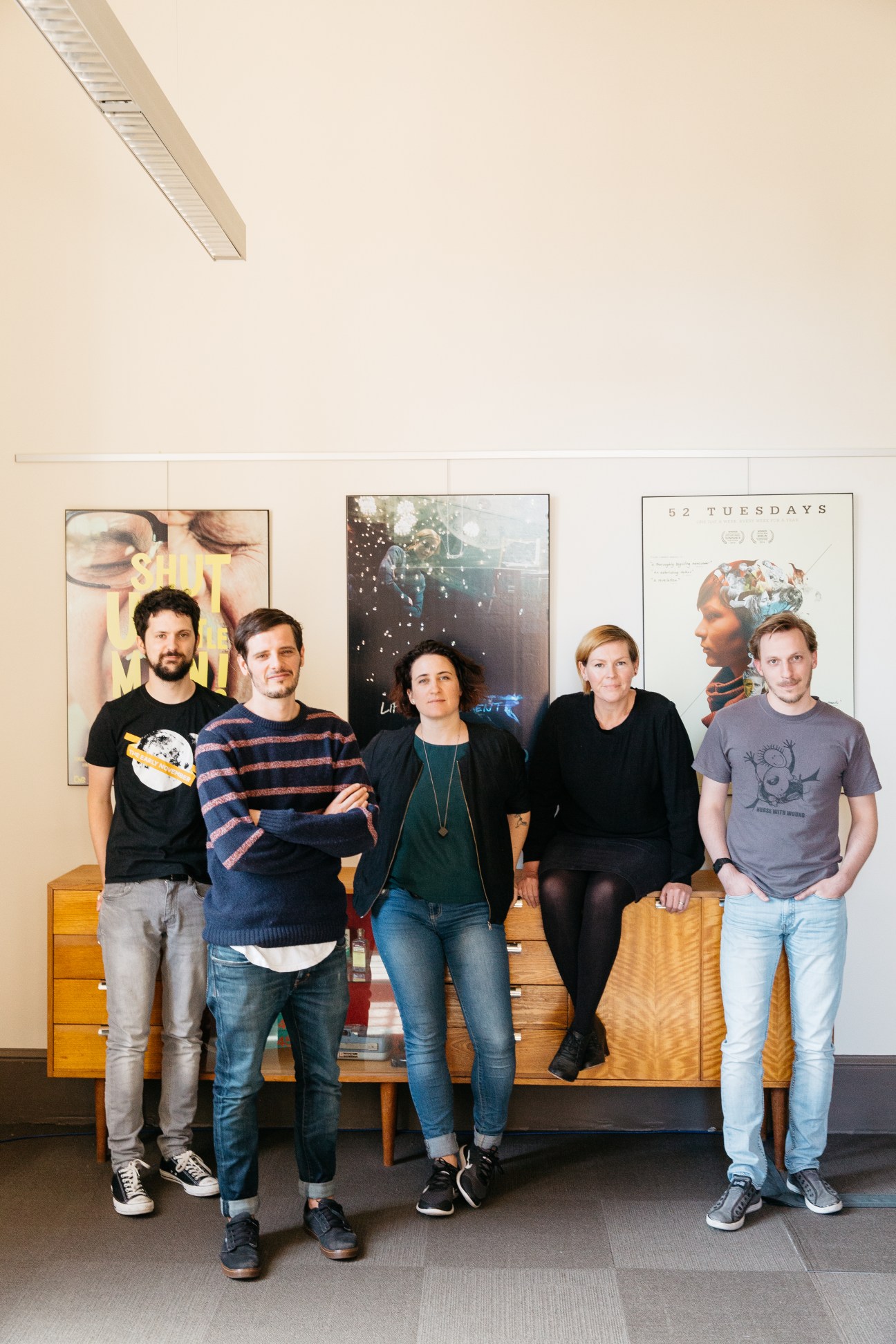 Five film professionals from Closer Productions stand in front of movie posters at Adelaide Studios.
