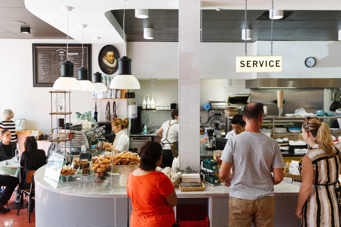 Interior of a modern café with customers at the counter and staff working in an open kitchen