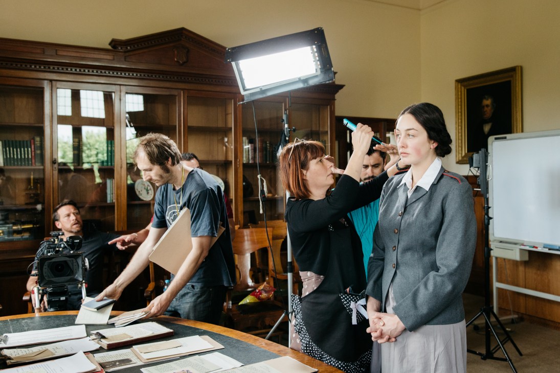 Film crew applying hair and makeup to an actress on set of 'Changed Forever' in a period room.