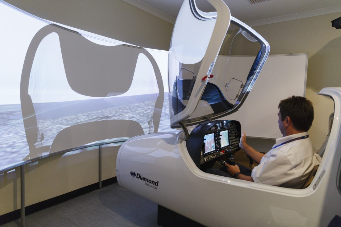 Pilot trainee in Diamond DA40 simulator with aircraft controls and flight display screen.