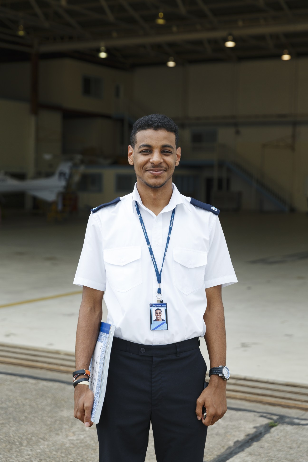 Twenty-year-old Tawfiq Jeneby, an FTA cadet, standing on the tarmac in uniform holding training materials.