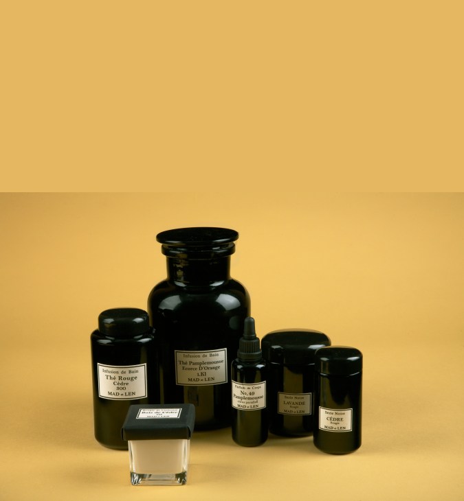 Mad et Len handmade bath and fragrance products in dark glass bottles against a yellow background.