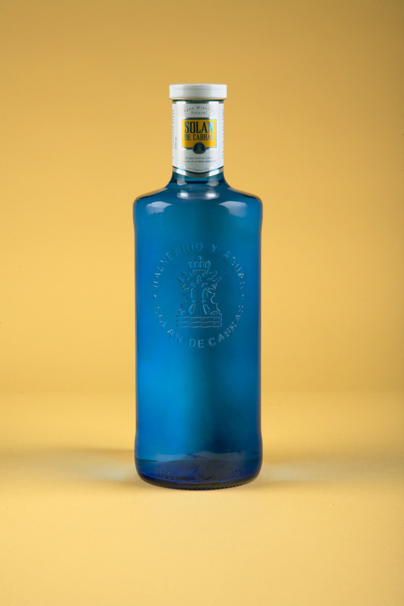 Solan de Cabras bottled water in heavy indigo-tinted glass against a yellow background.