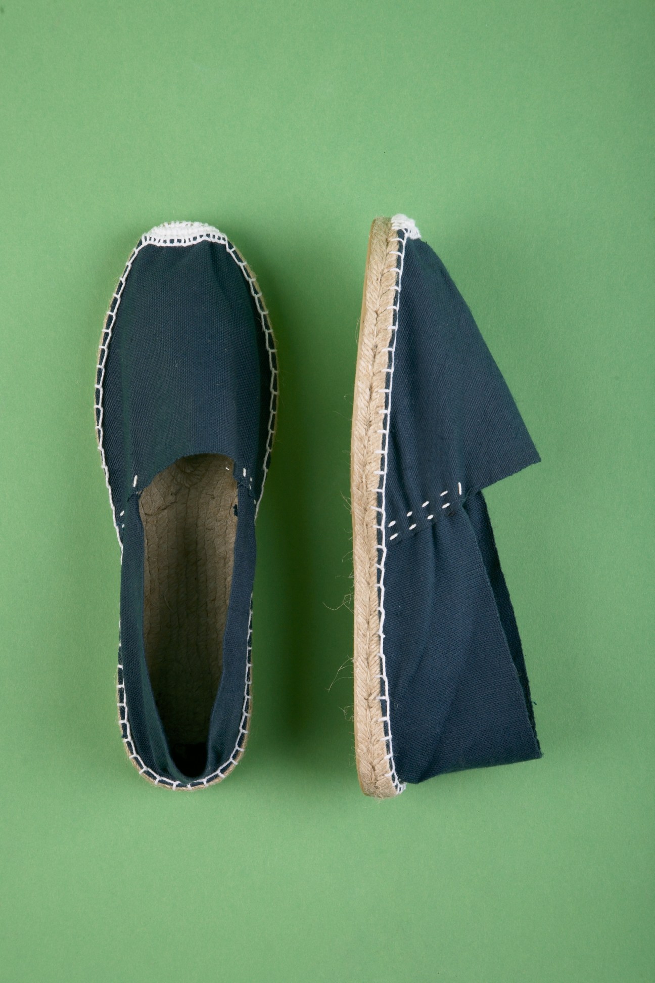 Pair of navy canvas espadrilles with jute rope soles displayed on green background.