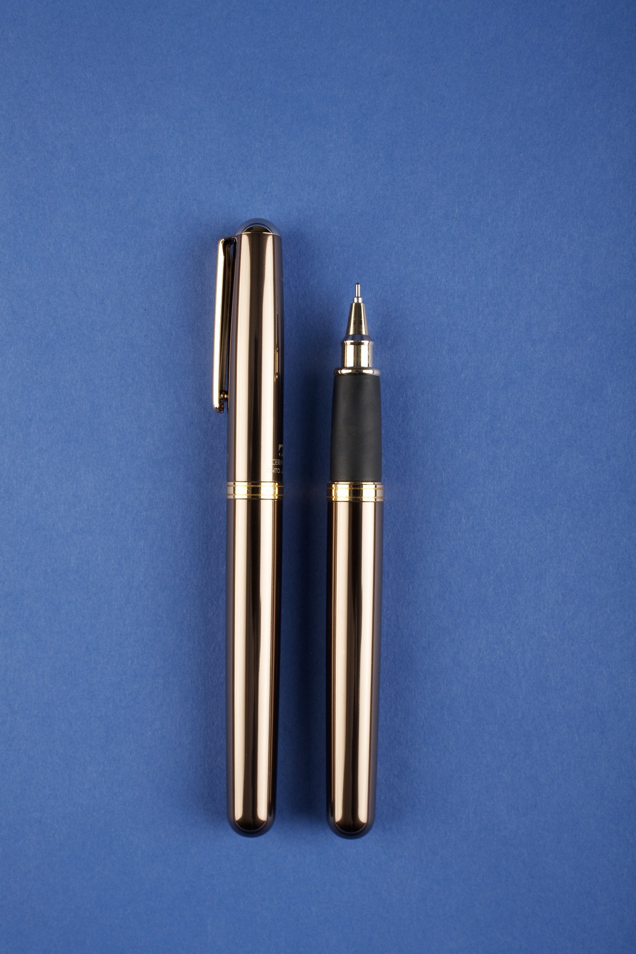 Two chrome and bronze Ohto pens with rollerball refills displayed on blue background.