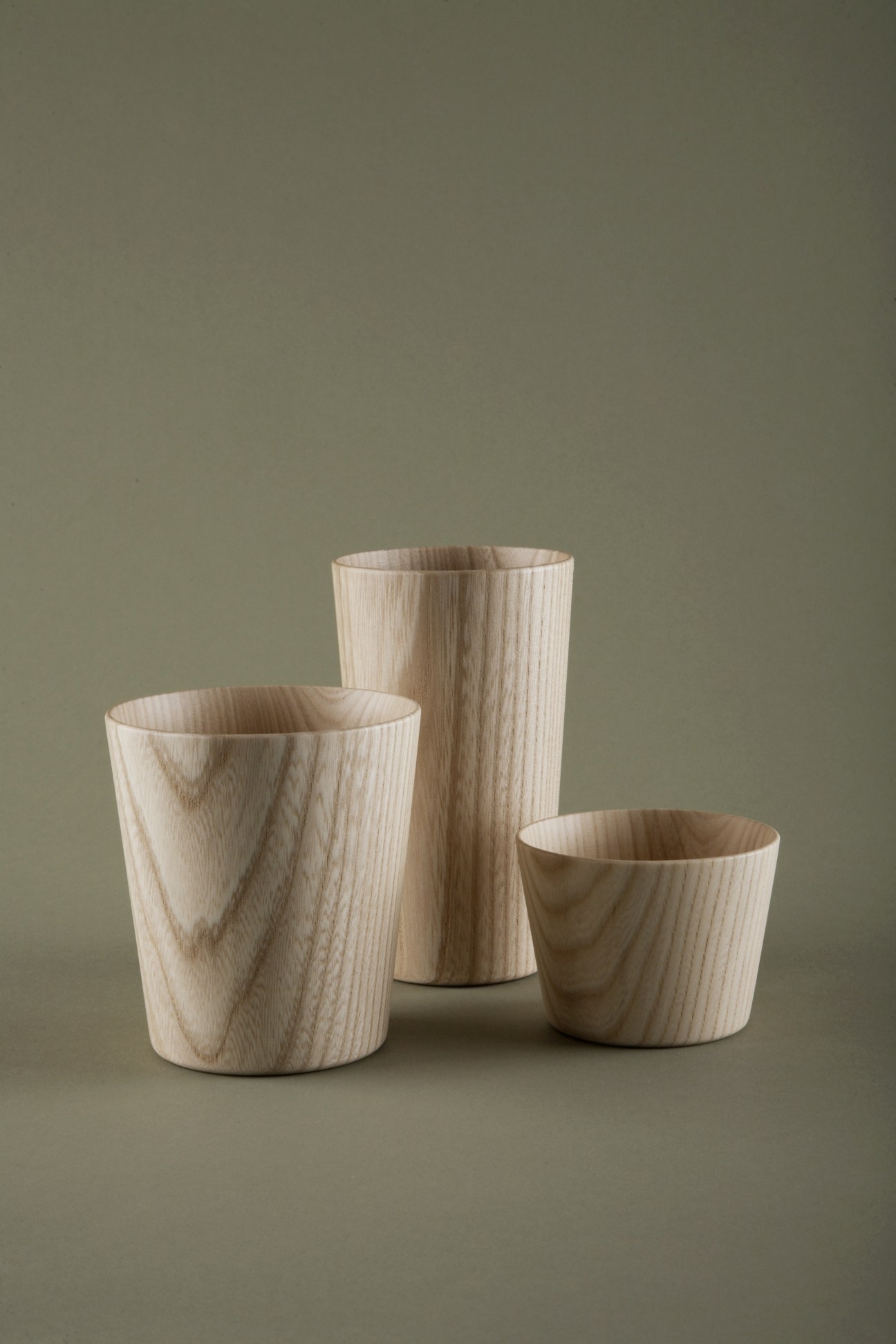 Three hand-crafted wooden cups in varying heights with natural light wood grain against a neutral background.