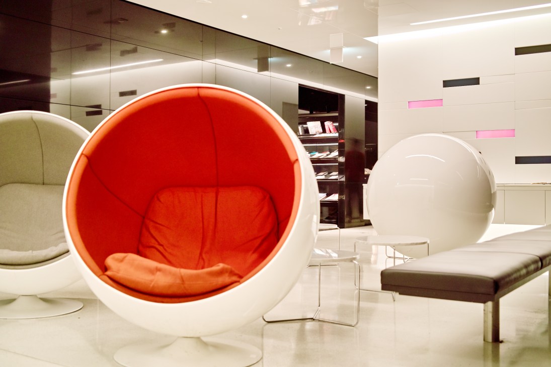 Modern lounge interior with spherical white pod chairs featuring red cushioned interiors, polished floors, and contemporary shelving.