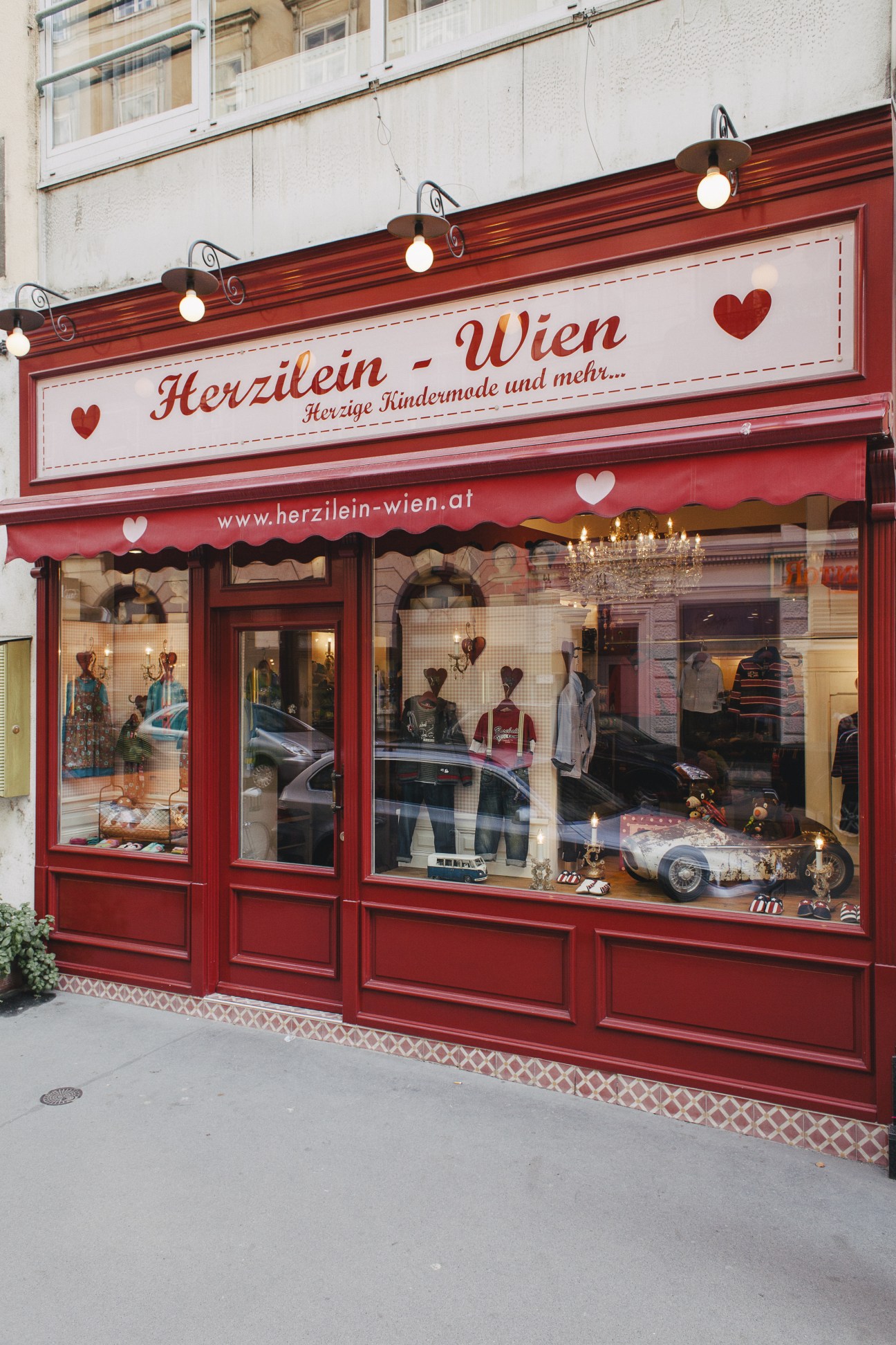 Red storefront of Herzilein Vienna children's clothing shop with heart decorations and window displays.