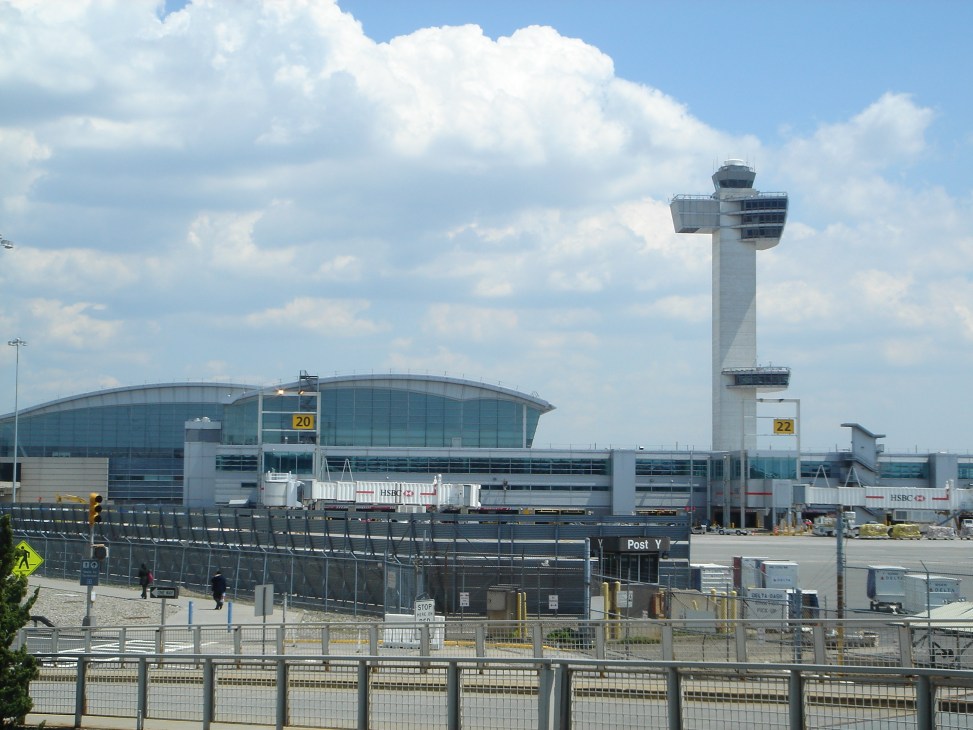 John F Kennedy International Airport's Terminal 4 with modern curved glass building and tall control tower.