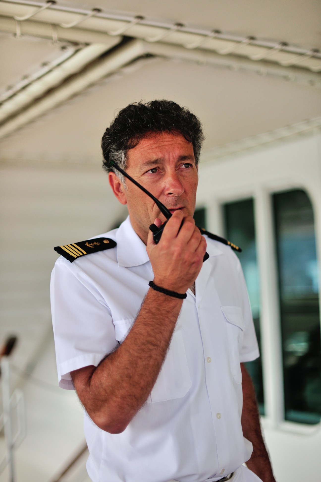 Captain Etienne Garcia in white uniform with captain's insignia holding radio headset aboard ship.