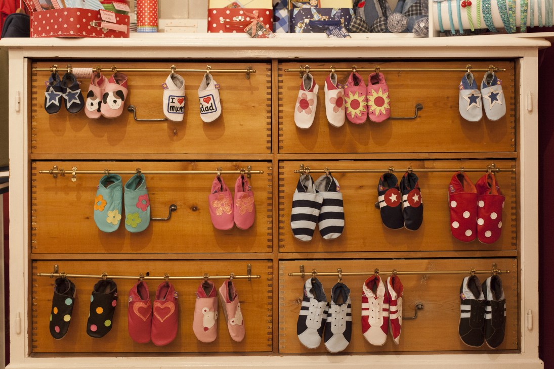 Wooden display cabinet with six compartments showcasing colorful children's slippers with various patterns and designs.