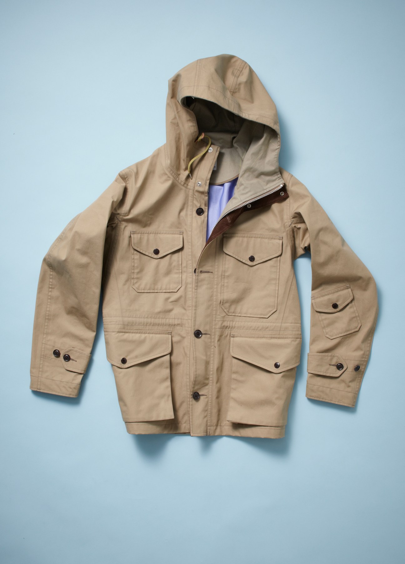 Beige field parka with hood and multiple chest pockets displayed against blue background.