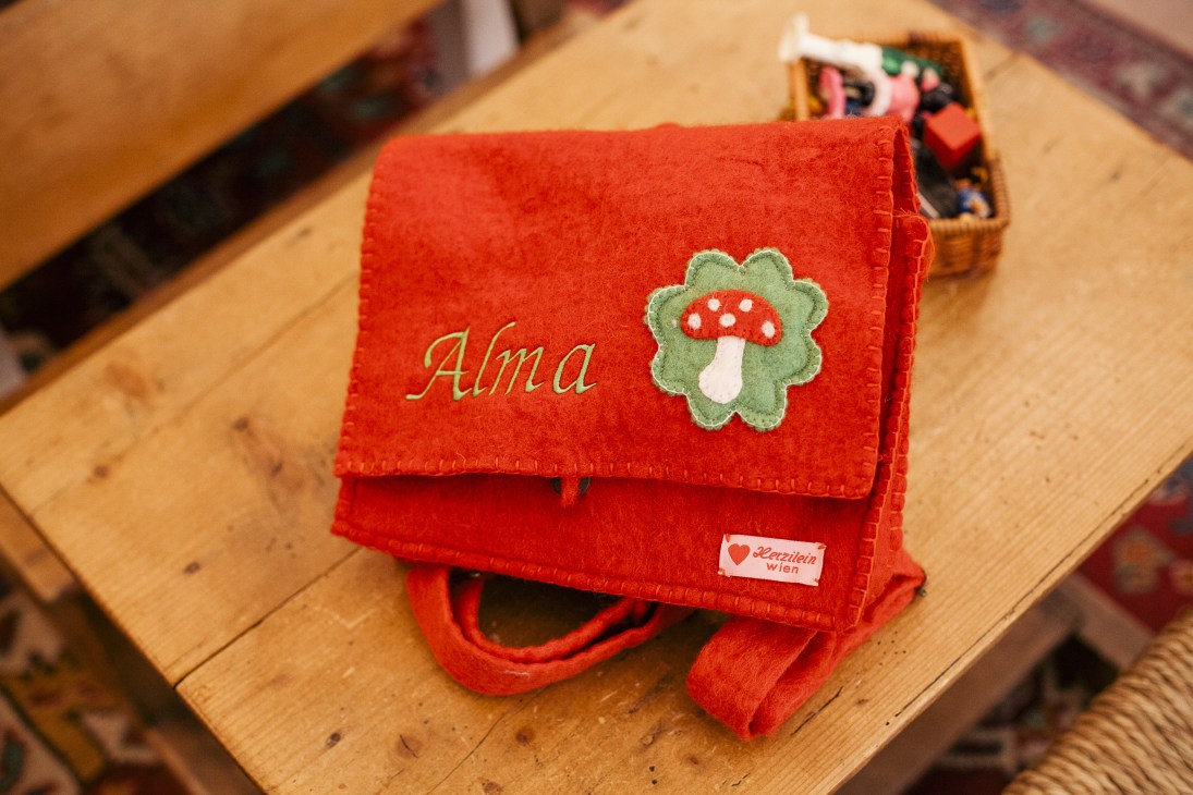 Red felt children's bag with personalized name embroidery and decorative mushroom appliqué.
